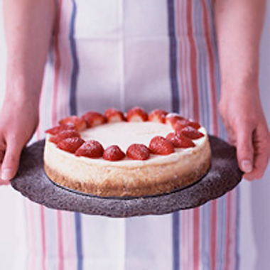 Anna, in an apron, holding her Real Cheesecake